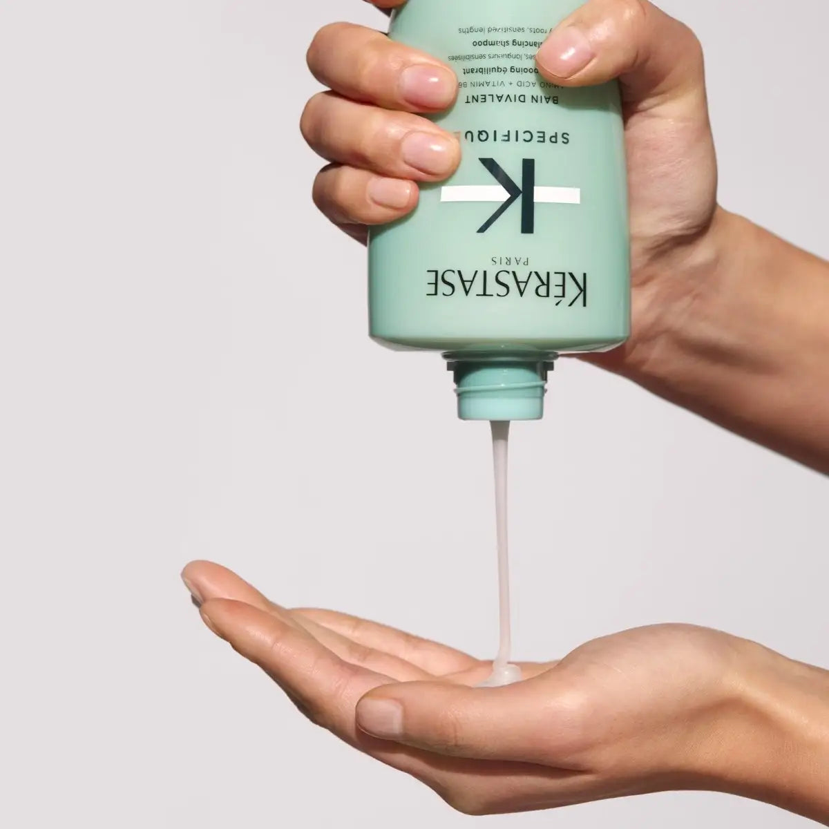 Mint green bottle of Kérastase Specifique Bain Divalent shampoo being dispensed into hand