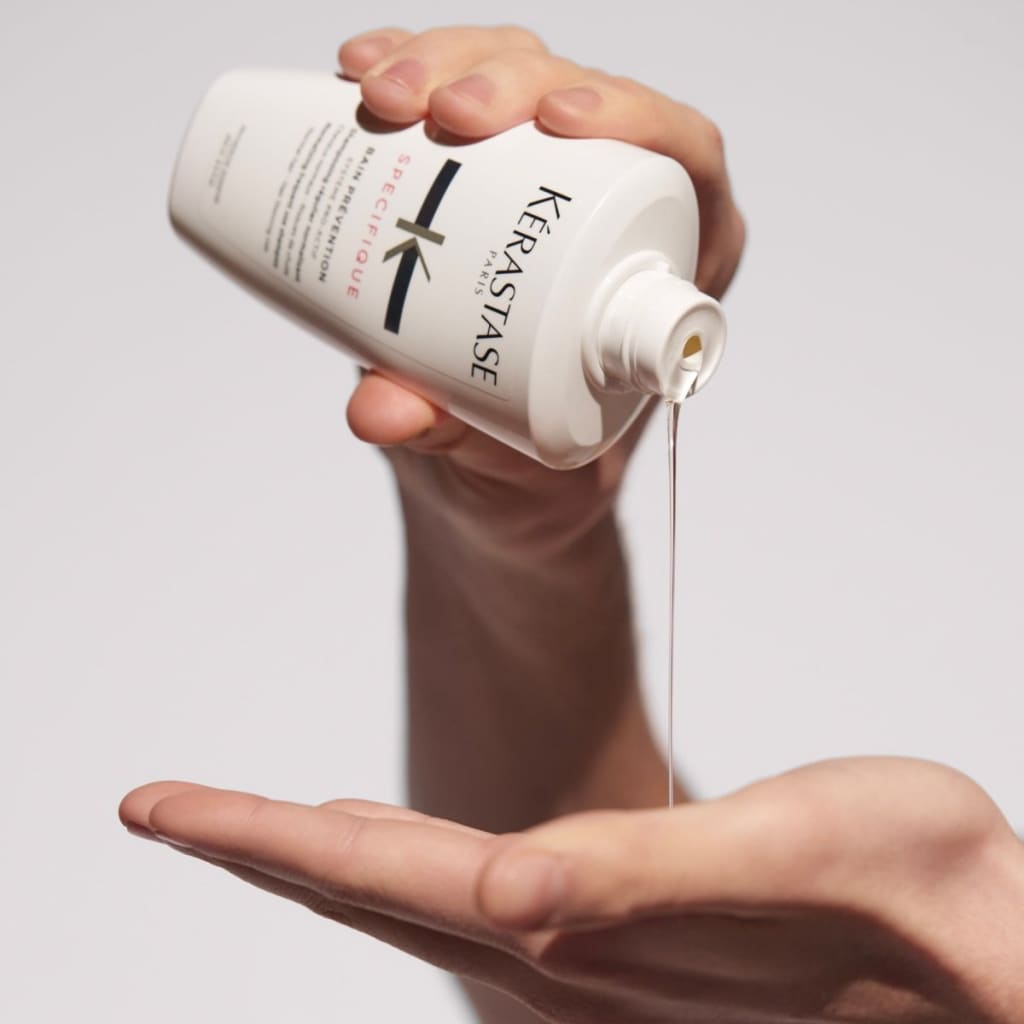 White bottle of Kerastase Specifique Bain shampoo being poured into a hand