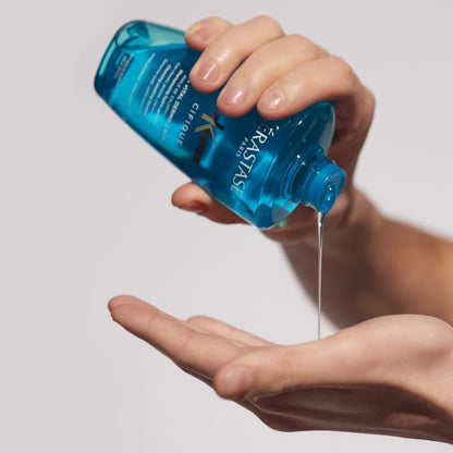 Blue bottle of Kerastase Specifique Bain Vital Dermo-Calm Shampoo poured into a hand