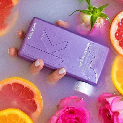 Kevin Murphy Hydrate.Me.Rinse 250ml with citrus, flowers, and manicured fingers holding the bottle