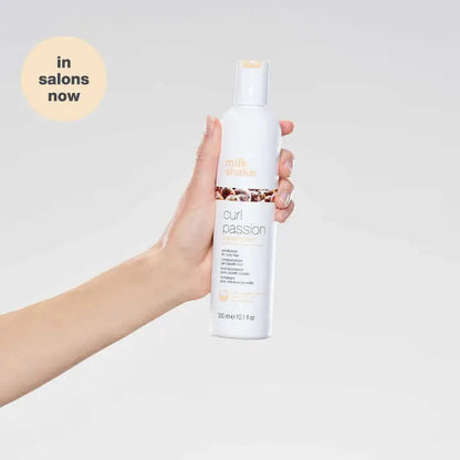 Hand holding Milkshake Curl Passion Conditioner bottle with white background and salon availability label