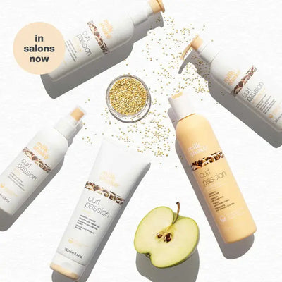 Milkshake Curl Passion Conditioner bottles and tube displayed with a sliced green apple and grains on white background