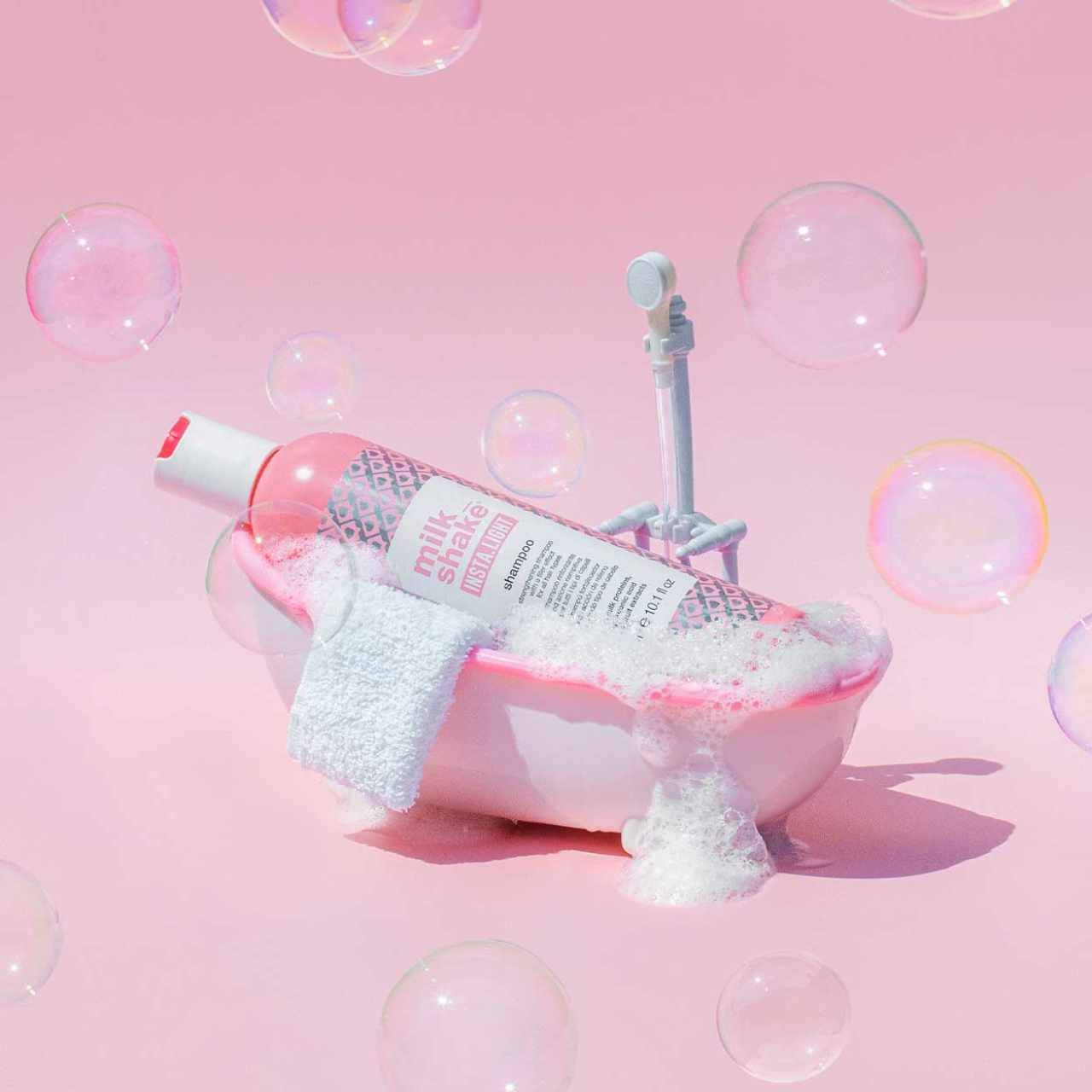 Milkshake Insta.Light Shampoo bottle in a small pink bubble-filled bathtub with white towel on pink background
