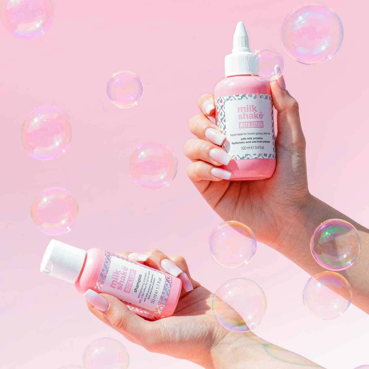 Milkshake insta.lotion conditioner in pink bottles held by hands with bubble background