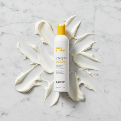 Milkshake integrity conditioner bottle with creamy texture spread on marble surface