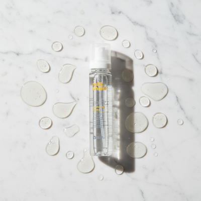 Milkshake no frizz glistening spray styling aid bottle with liquid droplets on marble surface