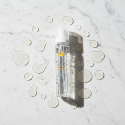 Milkshake no frizz glistening spray styling aid bottle with liquid droplets on marble surface