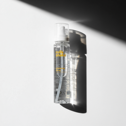 Milkshake no frizz glistening spray clear styling aid bottle with white spray cap casting shadow