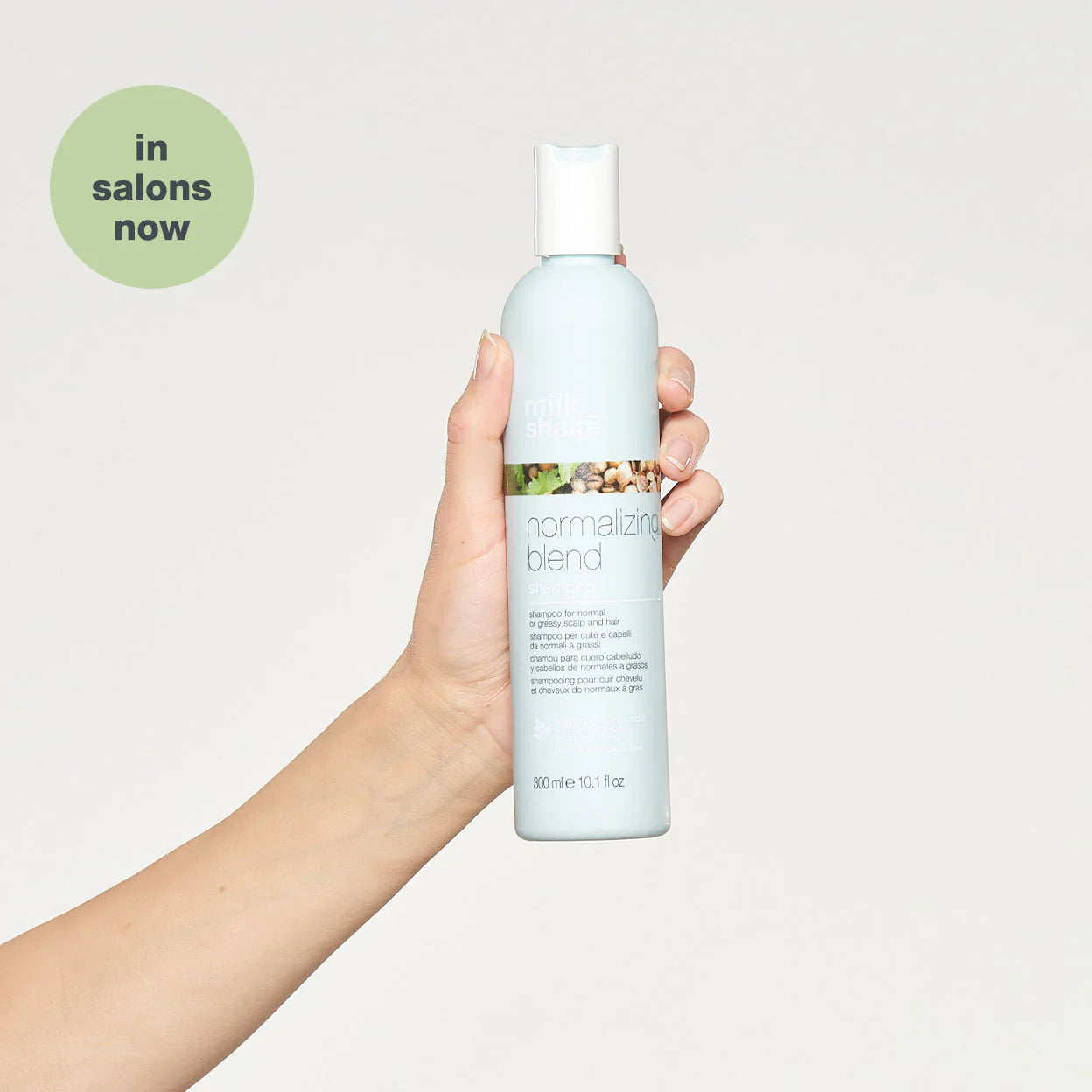 Hand holding Milkshake Normalizing Blend Shampoo bottle with light blue label and white cap