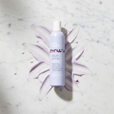 Milkshake Silver Shine light Shampoo bottle on marble surface with purple shampoo smear background