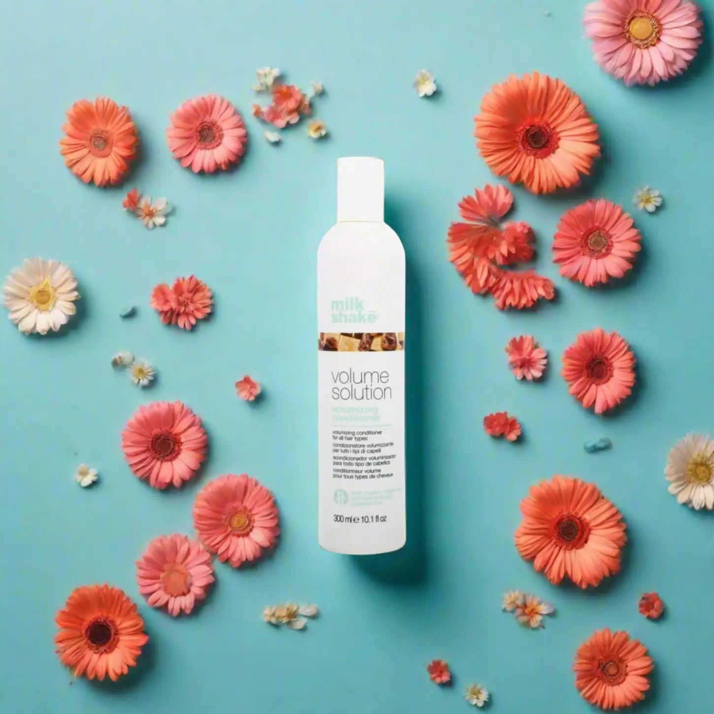 Milkshake Volume Solution Conditioner bottle surrounded by pink and orange flowers on a blue background