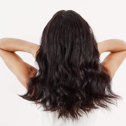 Long, wavy dark hair from behind showcasing Moroccanoil multitasking spray for unruly hair