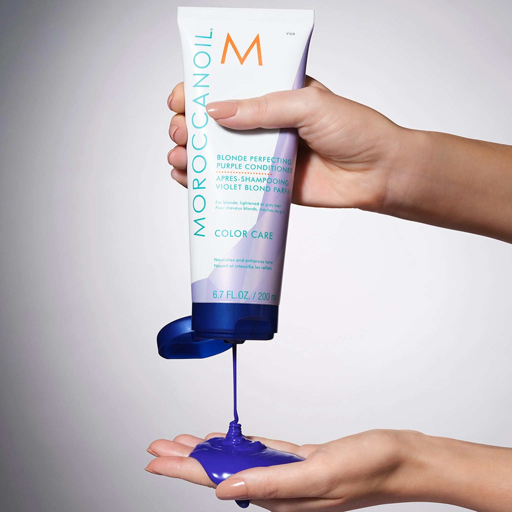 Moroccanoil Blonde Perfecting Purple Conditioner with vibrant blue liquid being squeezed out