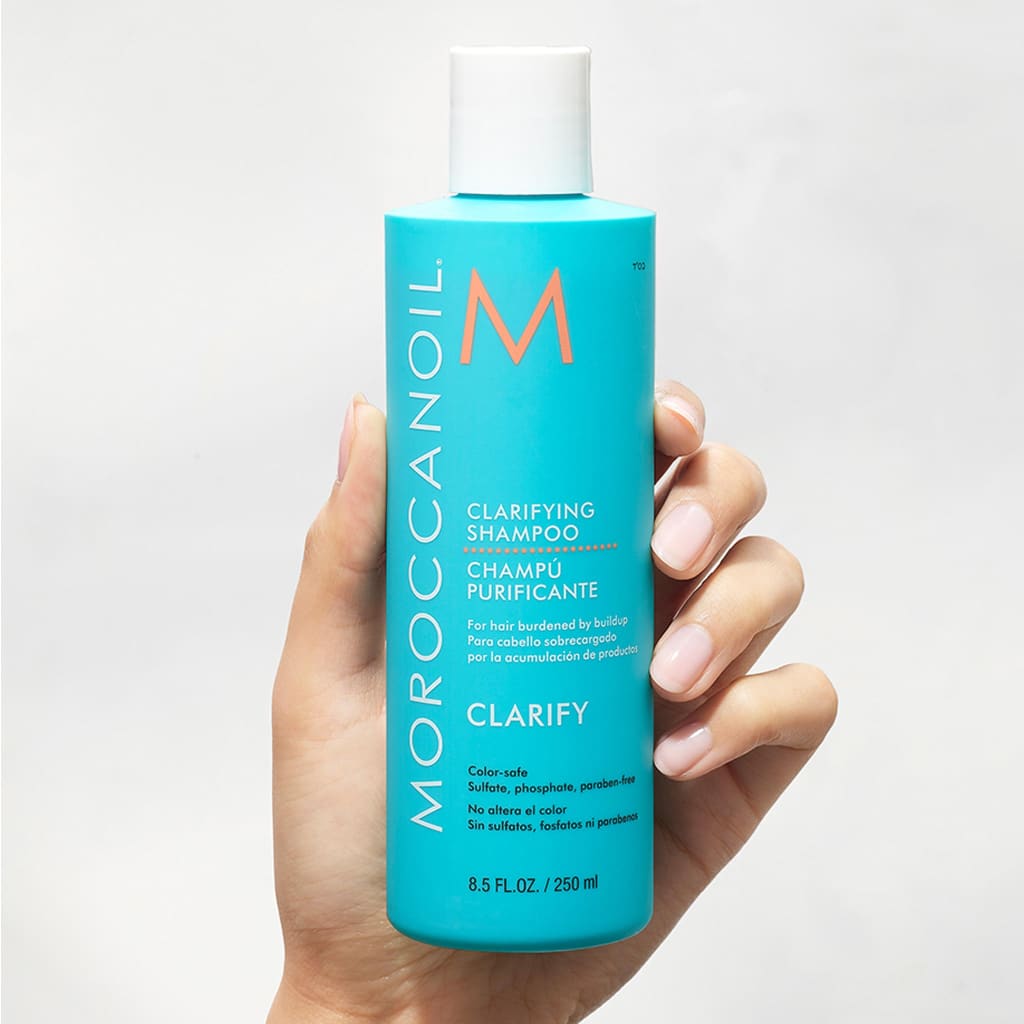 Hand holding a turquoise bottle of Moroccanoil Clarifying Shampoo 250ml removes everyday buildup