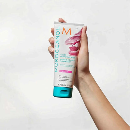 Hand holding Moroccanoil Color Deposit Mask Hibiscus tube hair treatment product with pink and turquoise design