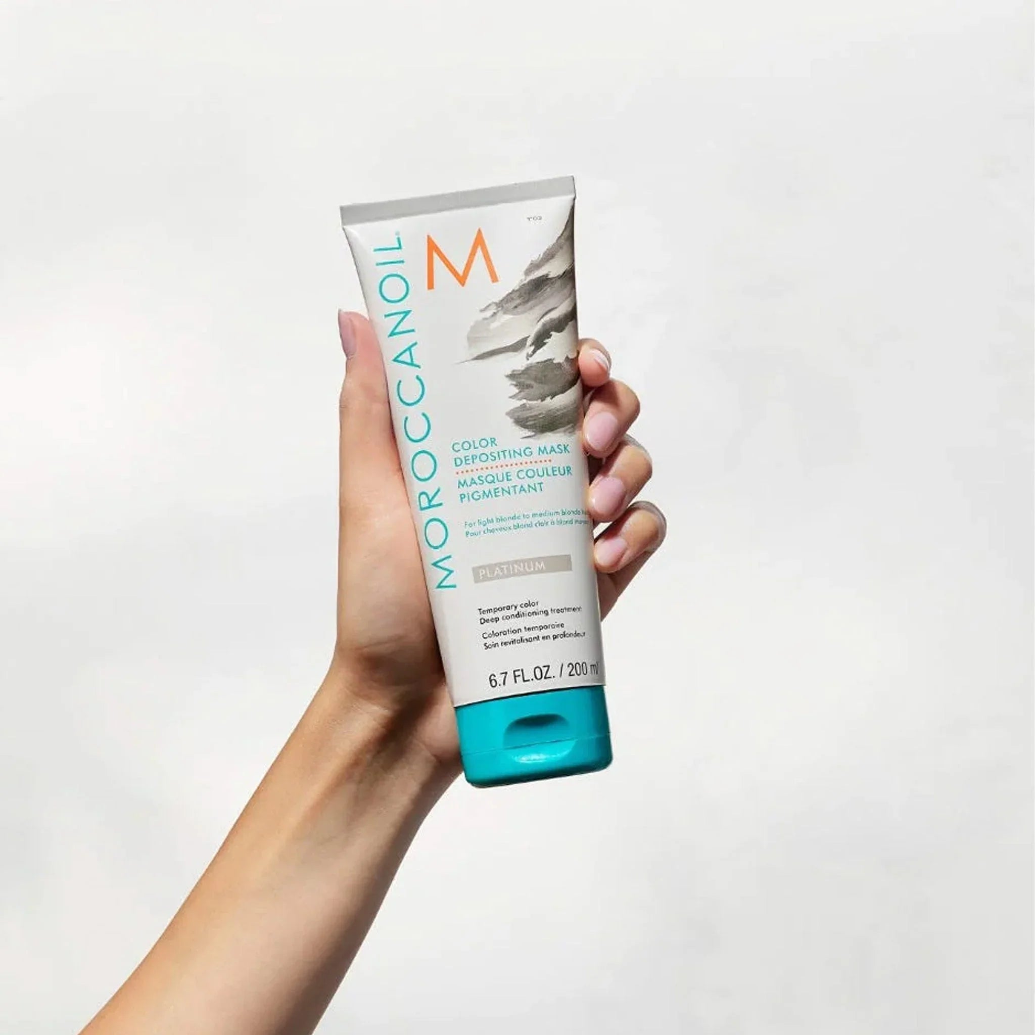 Hand holding Moroccanoil Color Deposit Mask Platinum 200ml for vibrant hair color
