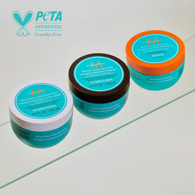 Moroccanoil intense hydrating hair mask jars in blue, black, and orange lids on a reflective surface PETA approved cruelty-free