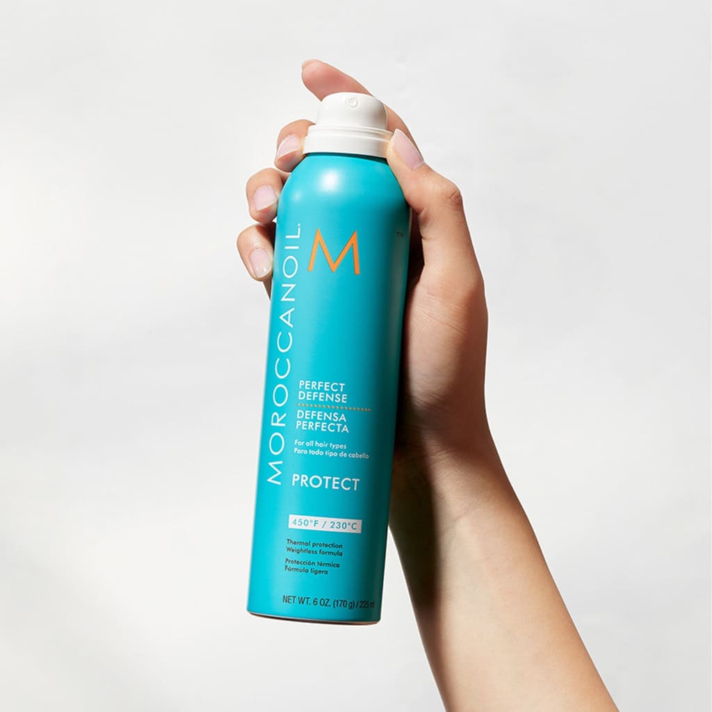Hand holding Moroccanoil Perfect Defense 225ml spray bottle with nourishing argan oil