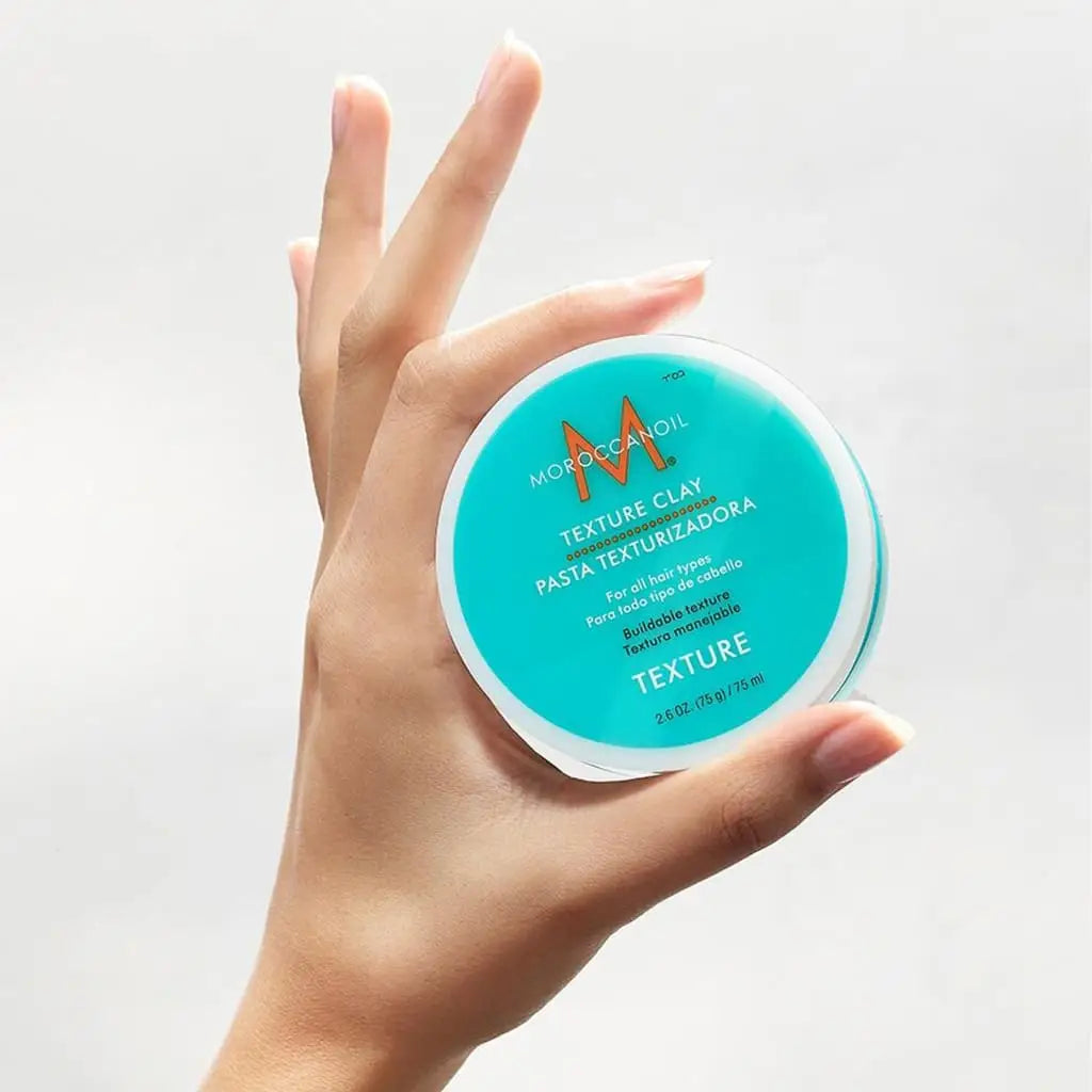 Teal container of Moroccanoil Texture Clay hair styling product held by a hand