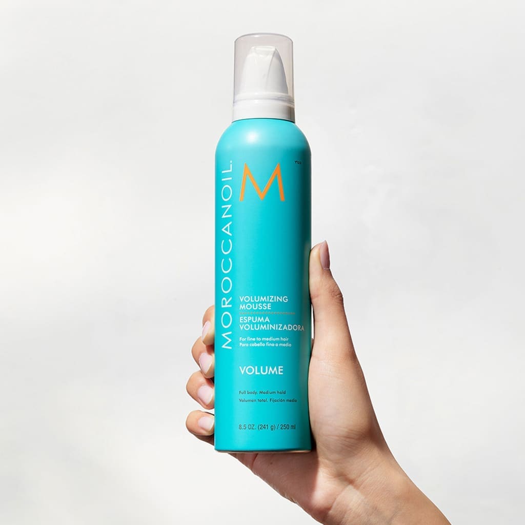 Hand holding Moroccanoil Volumizing Mousse 250ml for natural-looking styles