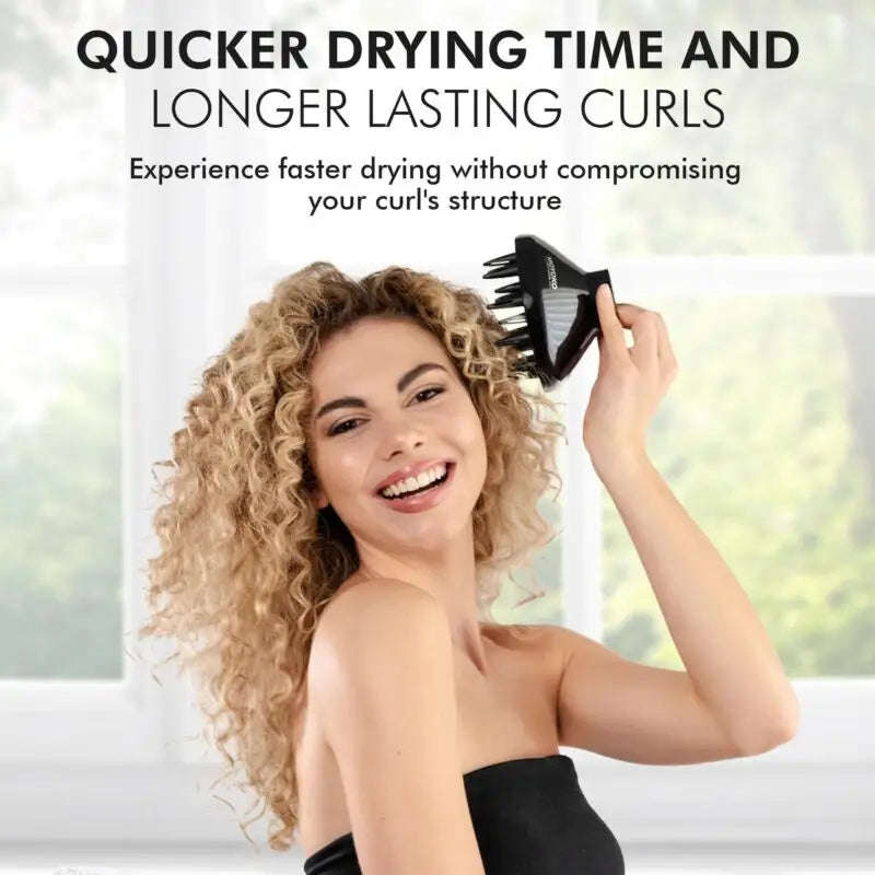 A smiling woman with curly blonde hair using a hair dryer.