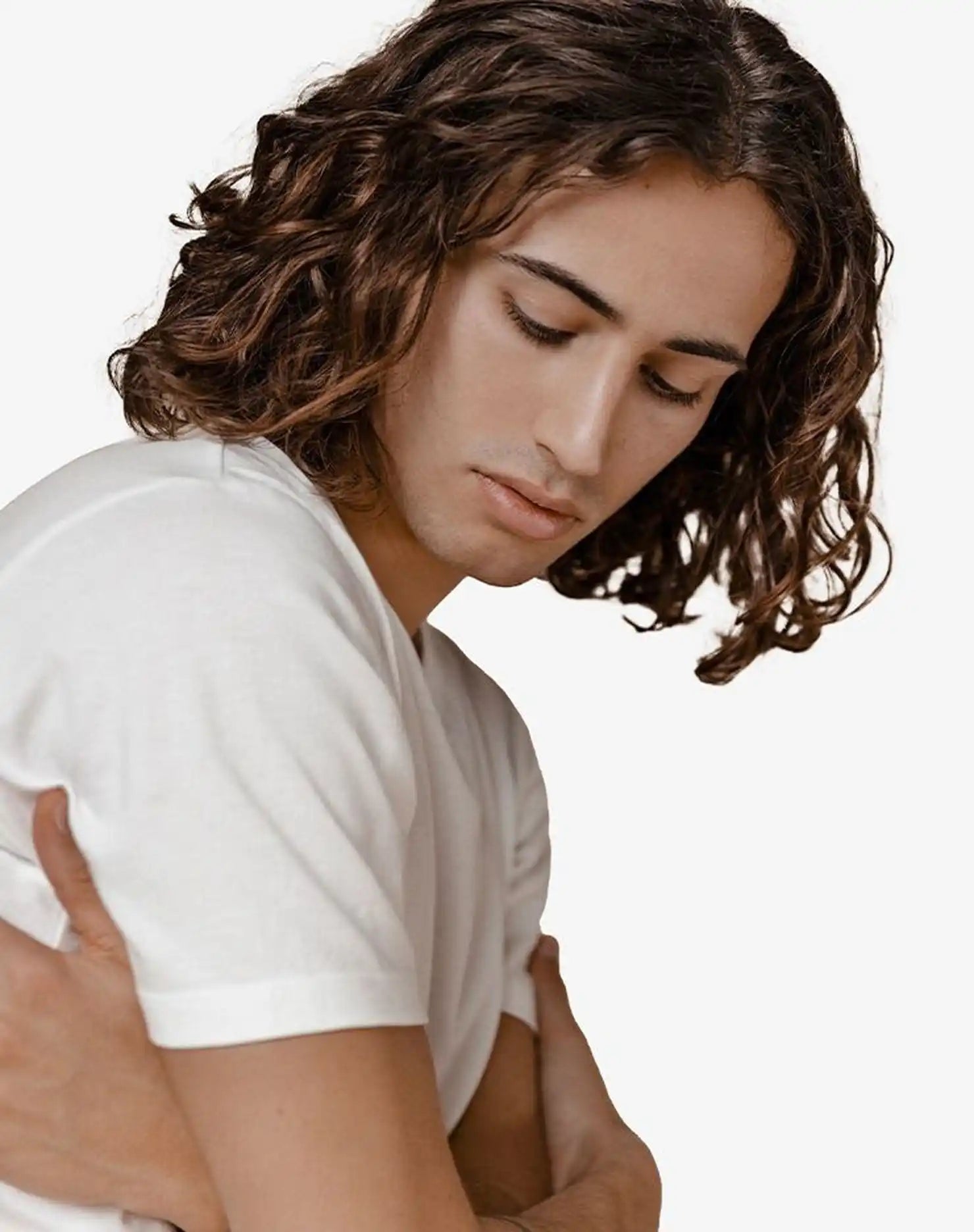 Person with curly brown hair wearing a white t-shirt, looking downward with eyes closed.