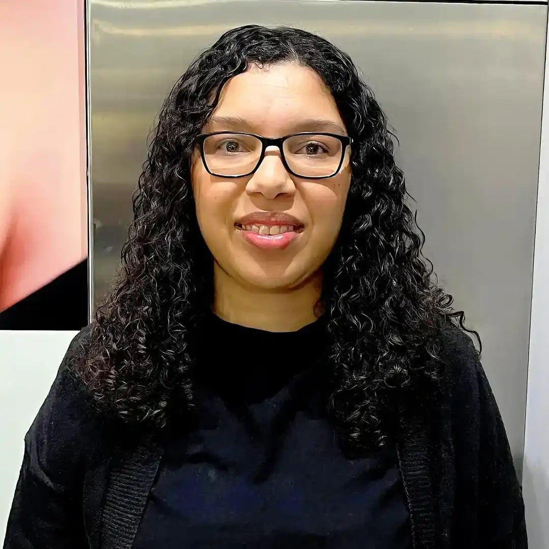 A smiling person with curly dark hair wearing glasses and a black sweater.