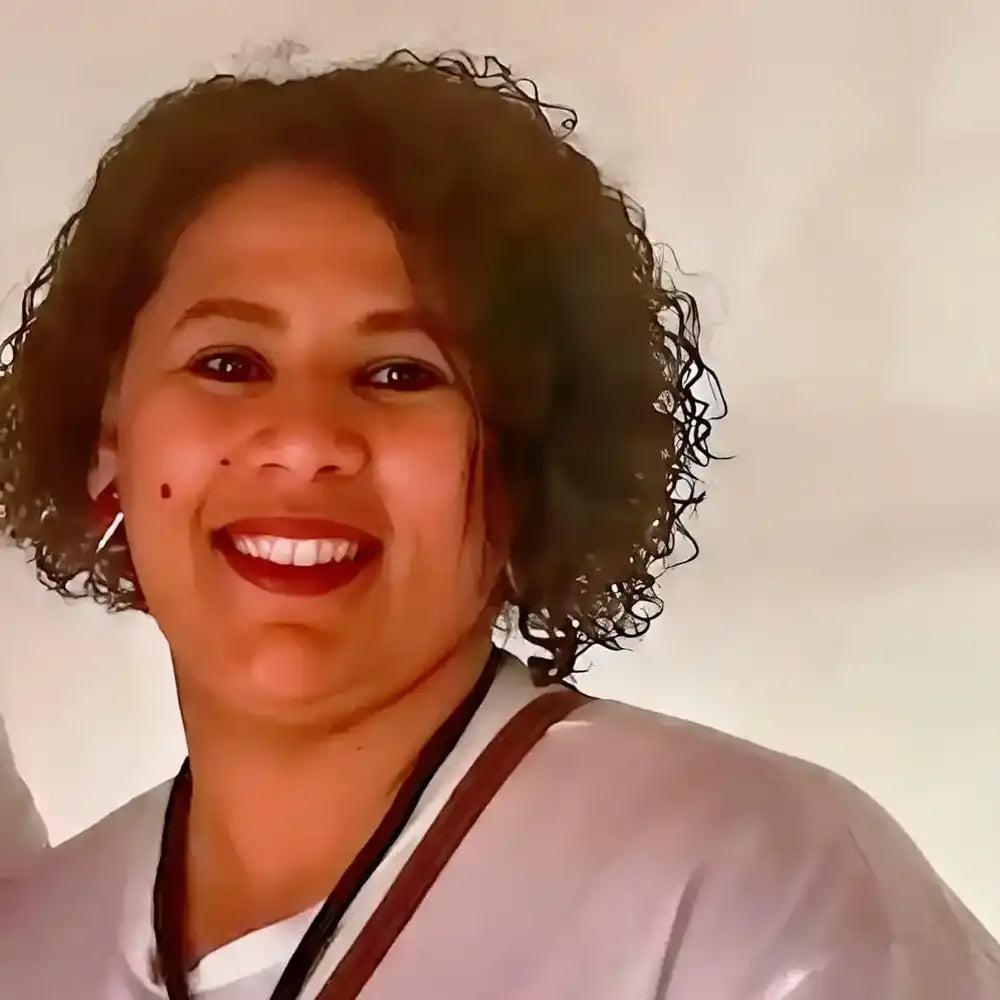 A smiling person with curly hair wearing a white top and red lipstick.