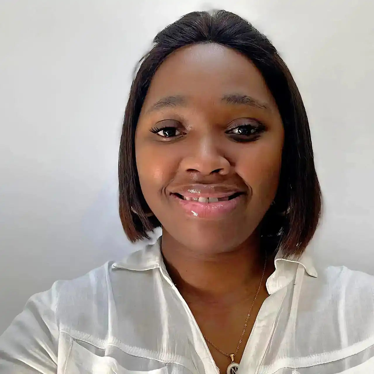 A smiling person wearing a white button-up shirt and a delicate necklace.