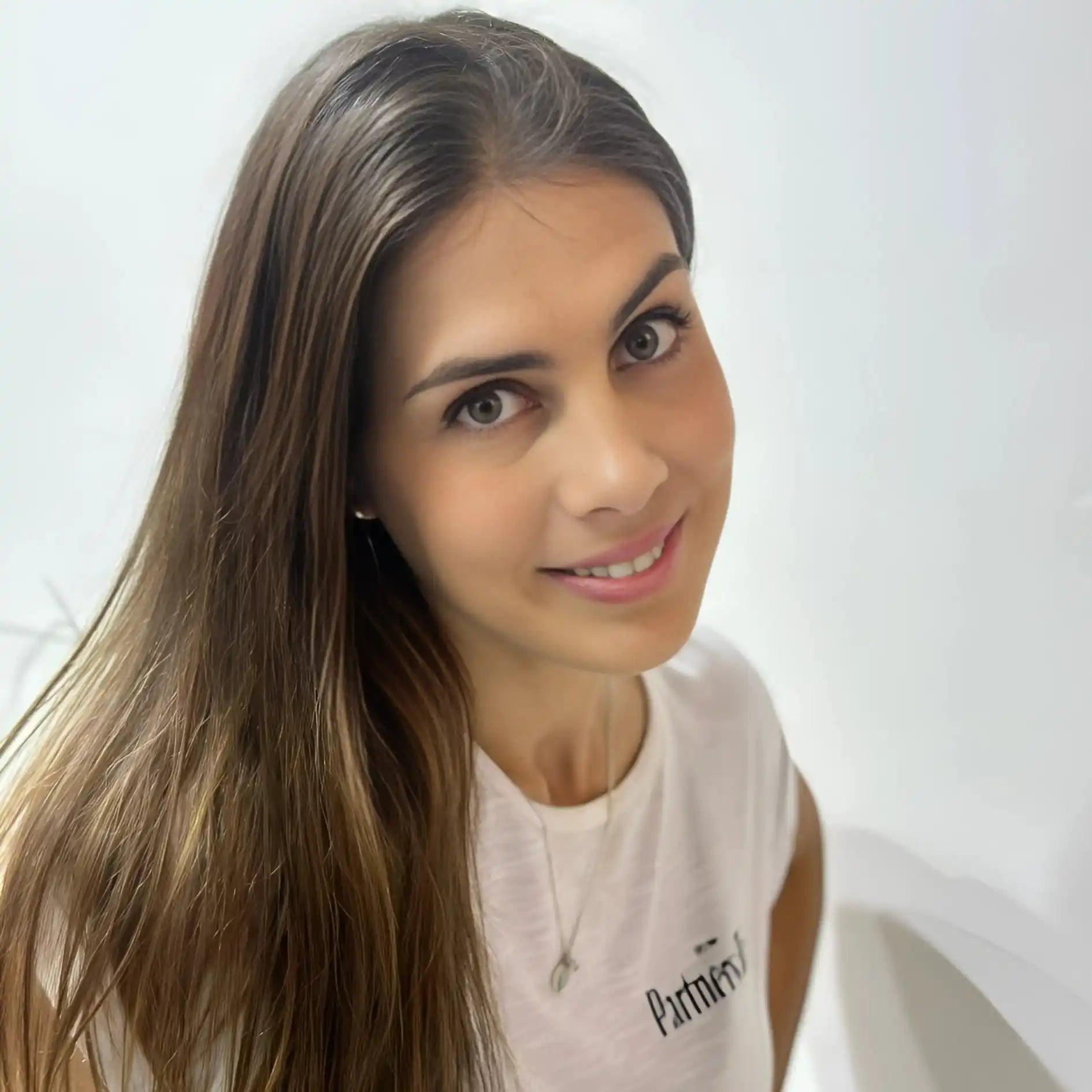 A smiling person wearing a white Puma t-shirt and small earrings.