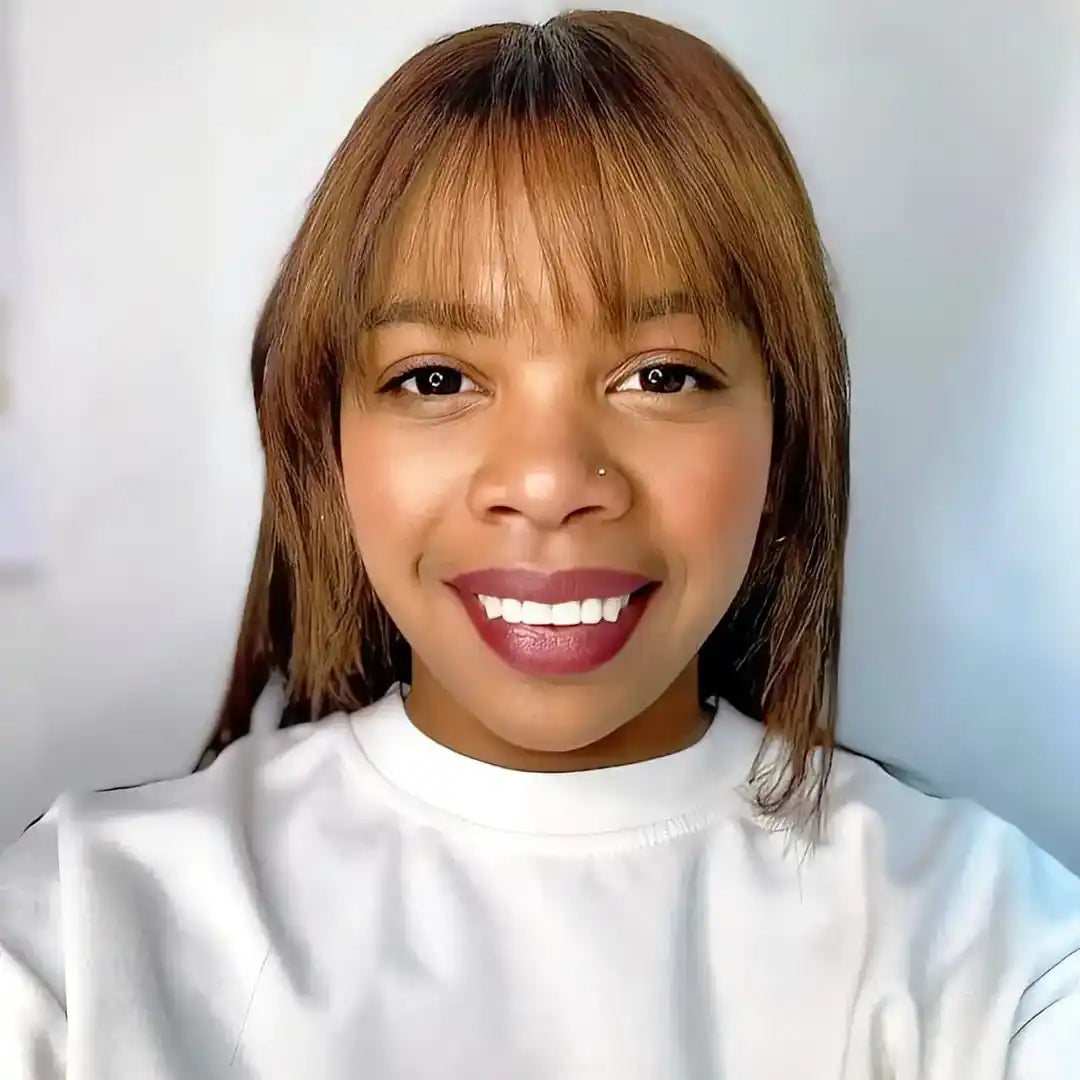 A smiling person wearing a white sweater with straight brown hair and bangs.