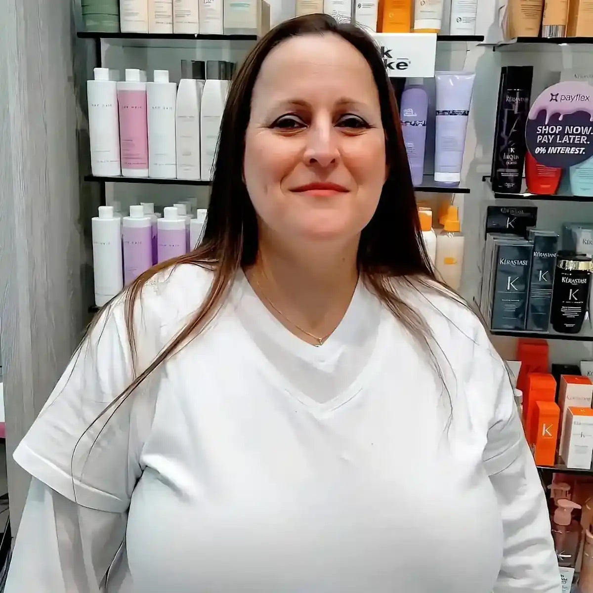 A person wearing a white uniform standing in front of hair product shelves.