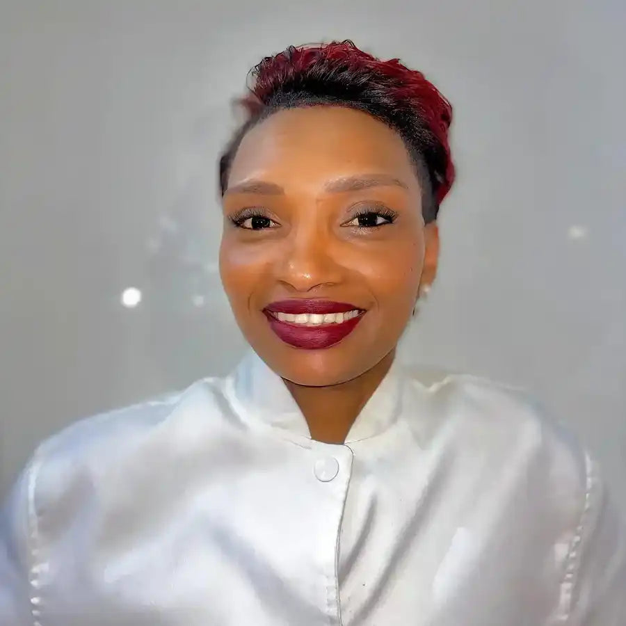 Professional headshot featuring a bright smile, red pixie haircut, and crisp white button-up top.