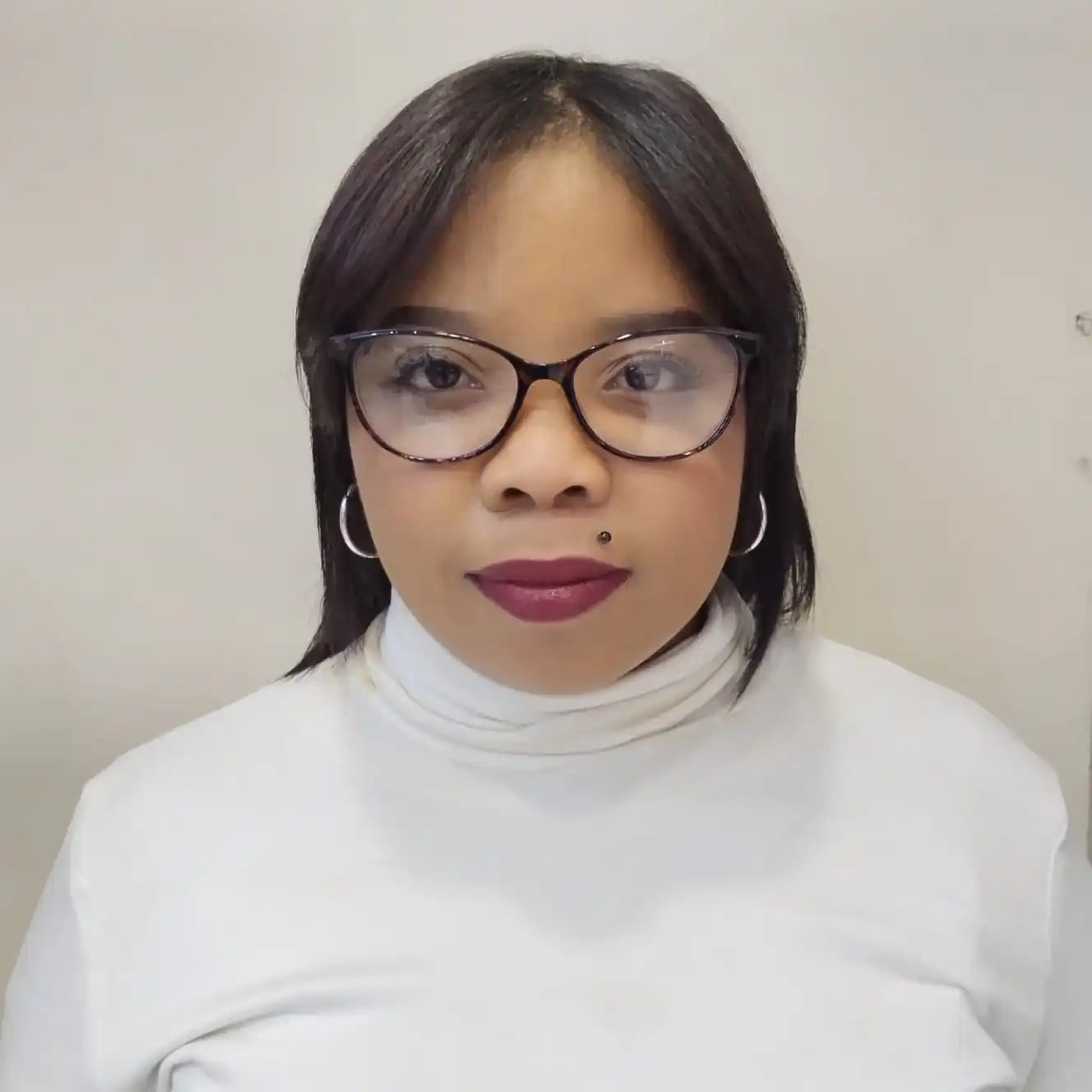 Professional headshot featuring cat-eye glasses, a white turtleneck sweater, and burgundy lipstick.