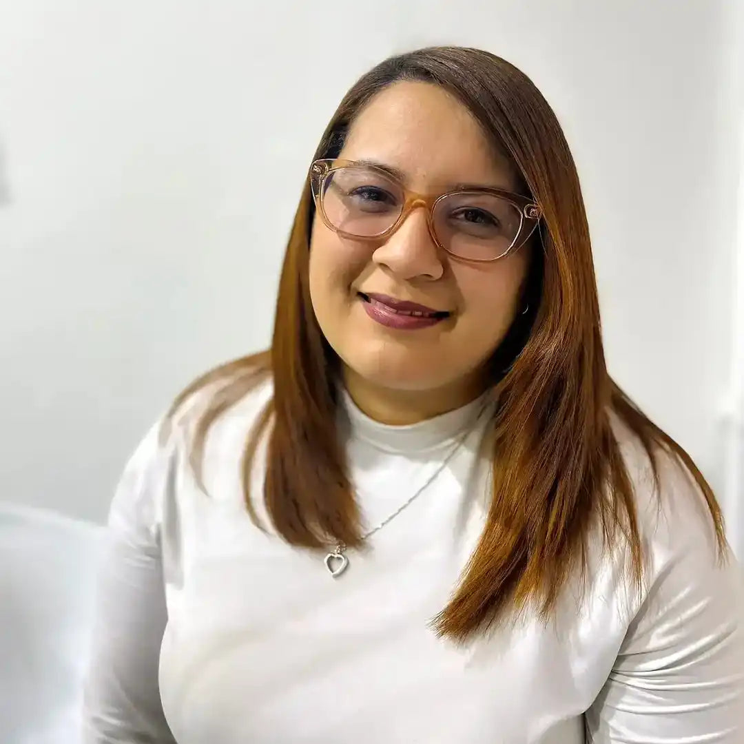 Professional headshot of someone wearing glasses, a white top, and a delicate necklace with straight brown hair.