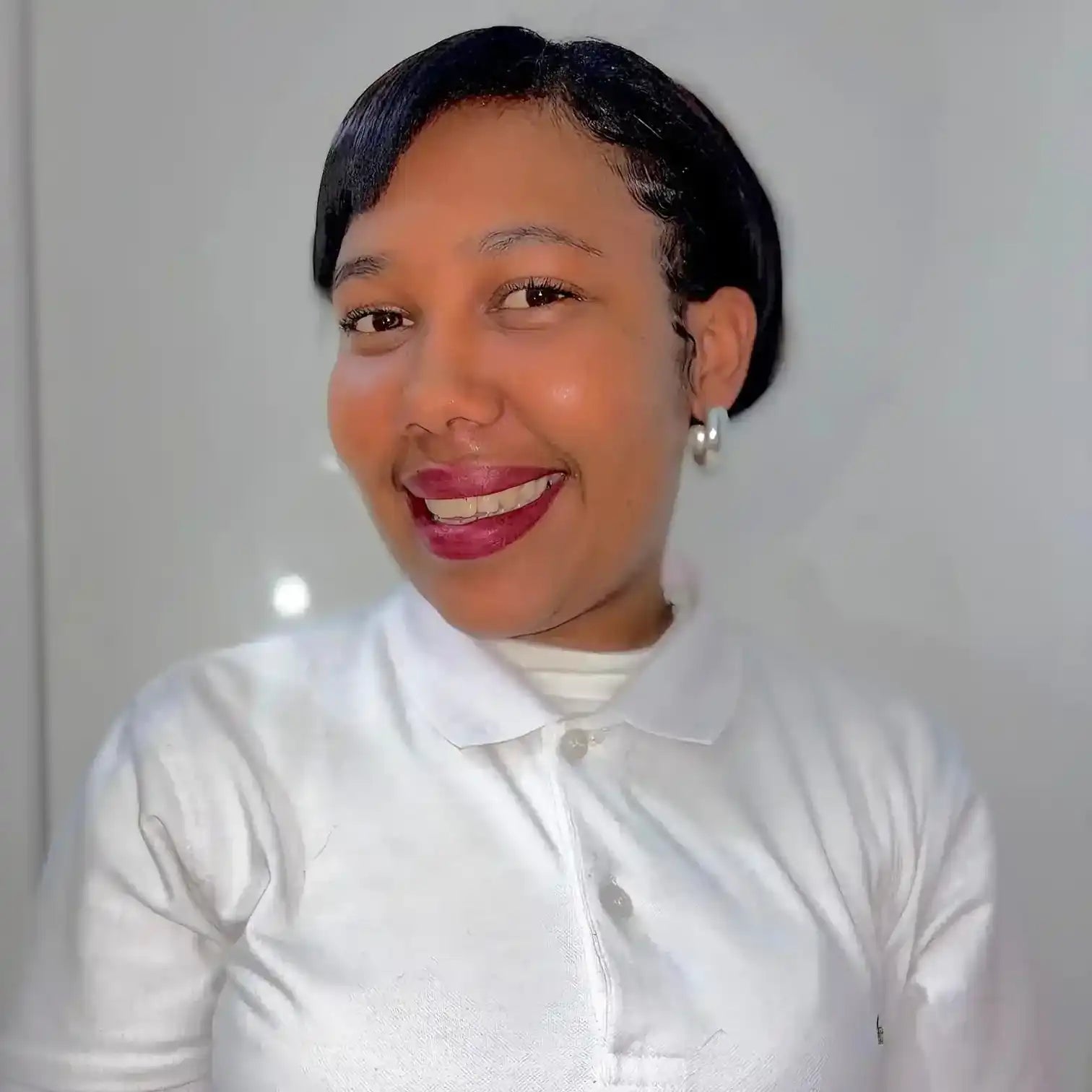 Professional headshot portrait showing a warm smile, white collared shirt, and burgundy lipstick.