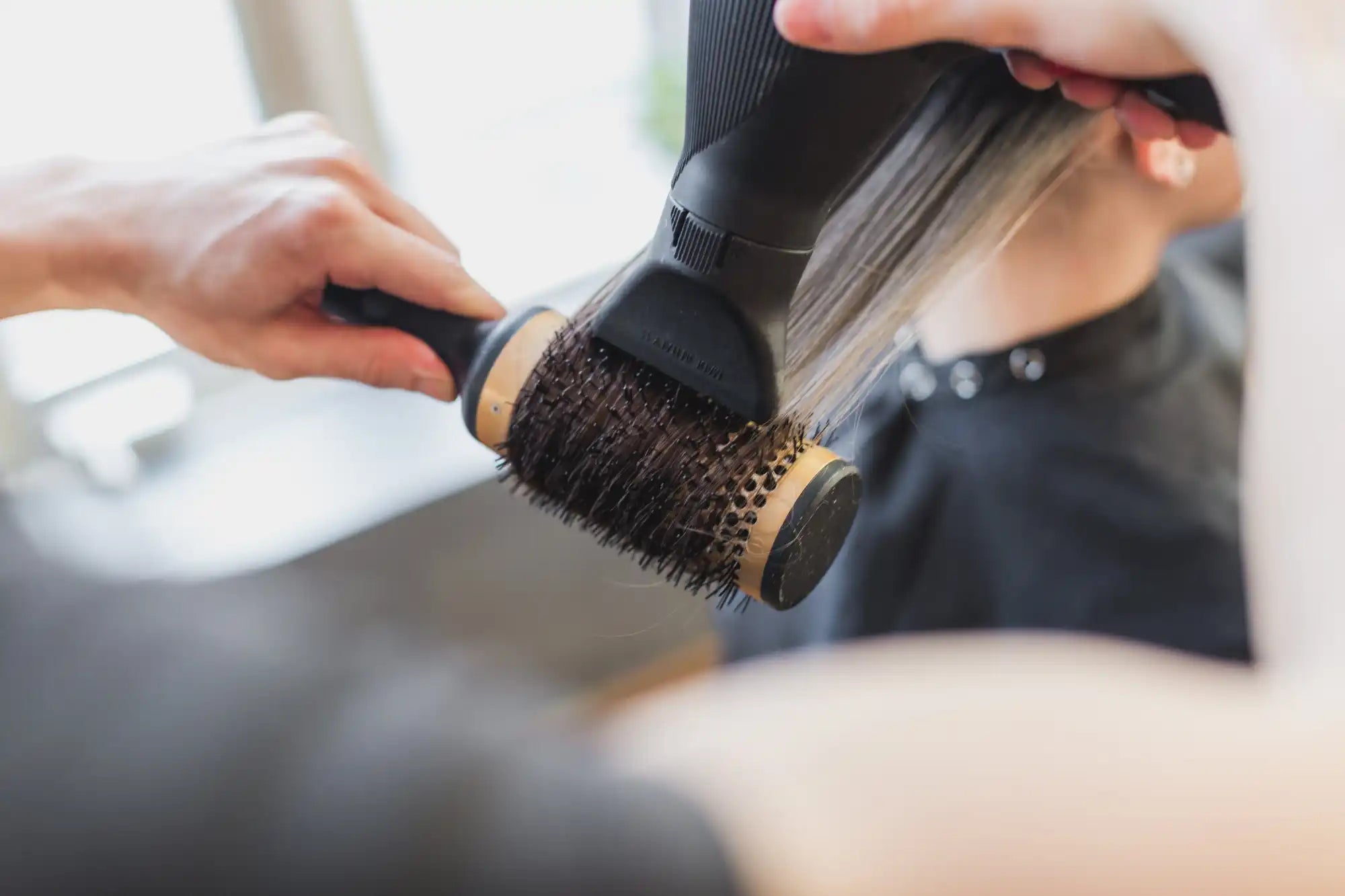 Round hairbrush being used with a hair dryer to style hair.