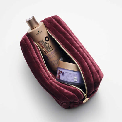 Burgundy velvet makeup bag or toiletry pouch with a zipper, partially open to reveal contents inside.