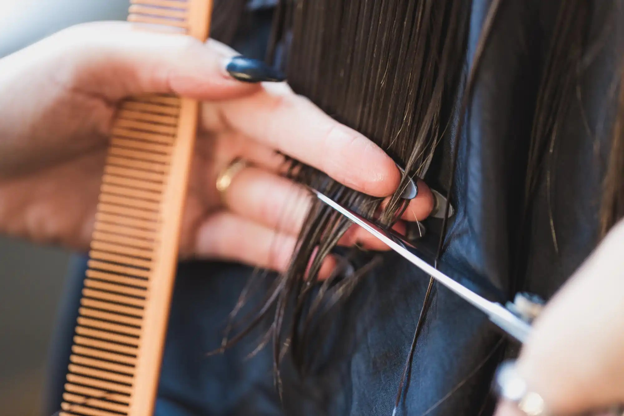 Scissors cutting dark hair while a comb is held nearby.