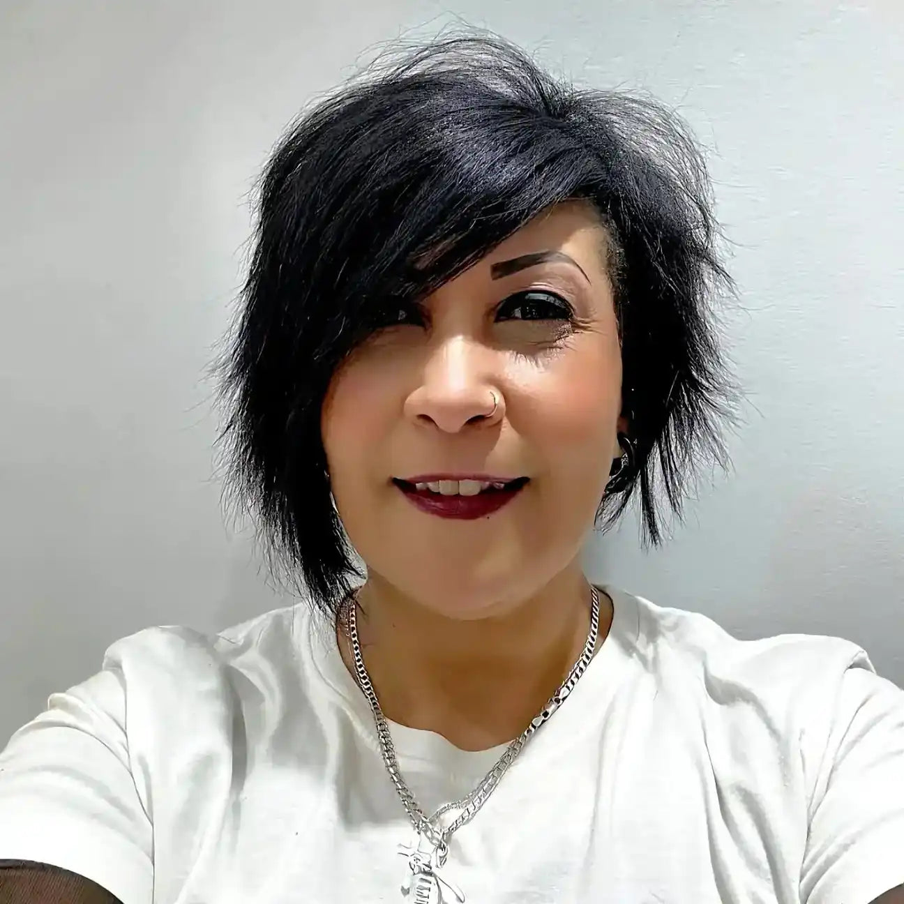 A selfie showing someone with dark spiky hair wearing a white top and dark lipstick.