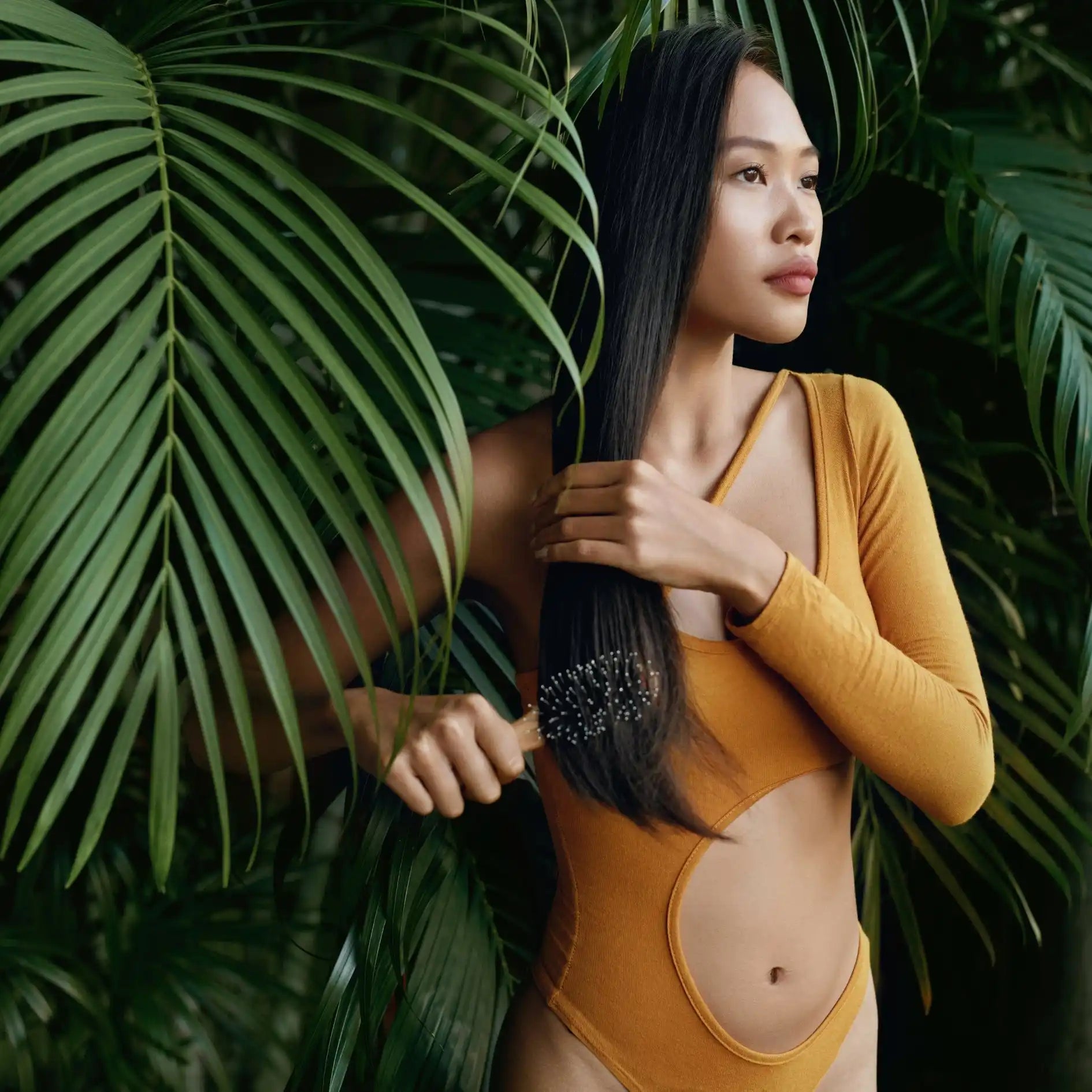 Woman with long dark hair wearing a yellow swimsuit surrounded by tropical foliage.